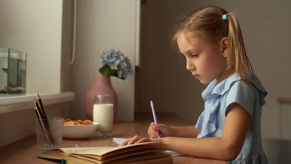 Closeup Side View of Concentrated Primary Child School Girl Writing to Notebook with Pen Looking on