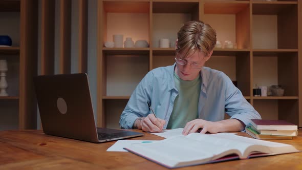 Guy Studying at Home Looks at a Laptop Writes a Notebook and Reads a Textbook