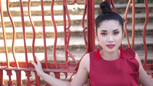 Beautiful Asian Woman In Red Suit Pose At Red Metal Fence