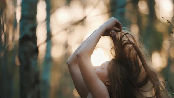 Young Caucasian Woman, Brunette Playing with Her Long Hair in the Forest on Sunset. Natural Beauty