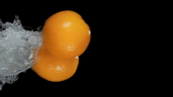 Two Oranges are Bouncing Horizontally with Water Splashes on a Black Background