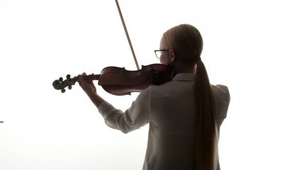 Woman Violinist in a White Blouse Plays the Violin Standing with Back on the White Background of