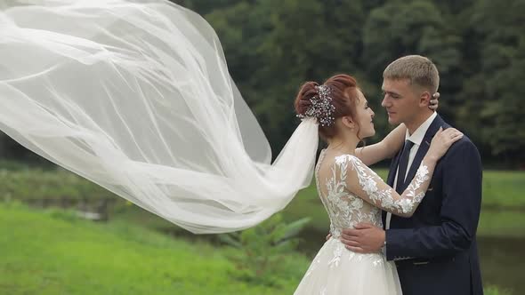 Groom with Bride in Bridal Veil Near Lake in the Park. Wedding Couple