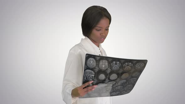 Young African American Female Doctor Looking at Xray While Walking on Gradient Background.