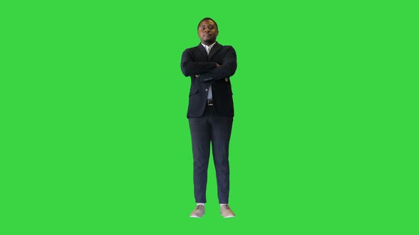 Young African American Man with Crossed Arms Pointing a Finger for the Camera on a Green Screen