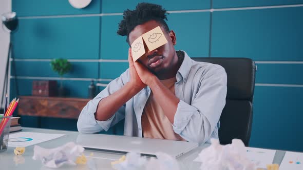 Young African American Man Office Worker Sleeps Sits at Desk in Office