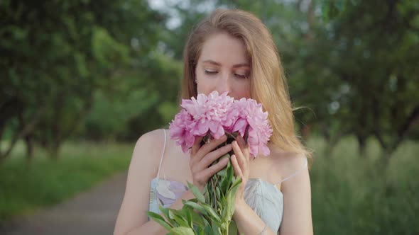 Beautiful Young Woman Smelling Bouquet of Flowers in Summer Park. Portrait of Charming Caucasian