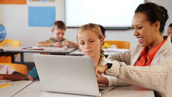 Teacher and schoolgirl using laptop in classroom