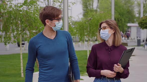 Two work colleagues in protective mask walk outside office building.