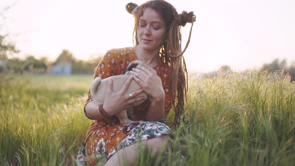 Beautiful Hippie Woman with Dreadlocks in Green Grass with Her Puppy of Pugdog at Sunset Having Good