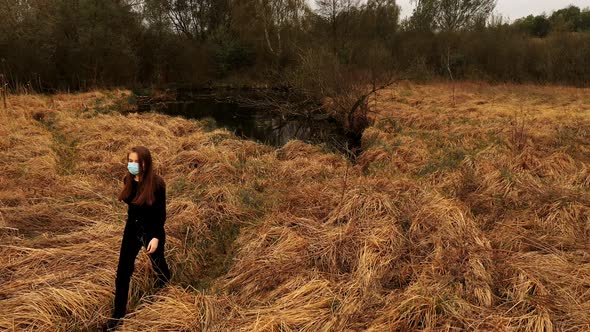 Woman in Protective Mask Goes By Path of Orange Grass