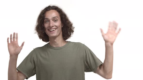 Attractive Young Hipster Guy with Wavy Messy Hairstyle Wearing Tshirt Waving at Camera with Friendly