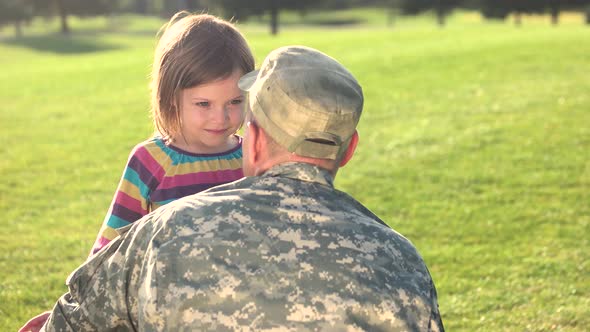 Soldier in Camoubackgrounde Hugging His Daughter in the Park.