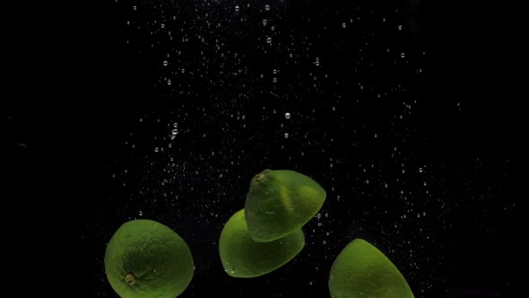 Slow Motion Green Lime Halves Falling Into Transparent Water on Black Background