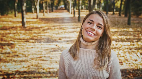 Young Woman Smiling Straightening Her Hair and Looking Shy Flirting with you While Posing at Autumn