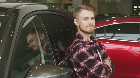 Handsome Man Showing Thumbs Up Leaning on a New Car at the Dealership