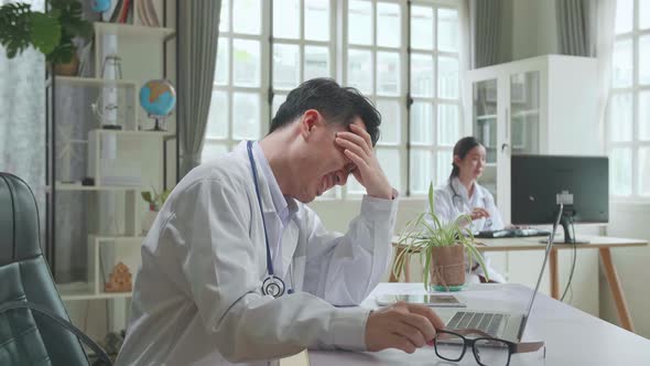 Asian Man Doctor Is Using Laptop Computer And Headache In Workplace. Medical Concept