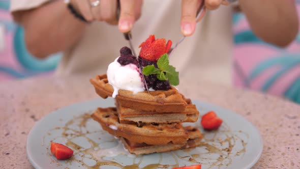 Female Hands Cutting a Stack of Belgian Waffles Topped with Ice Cream with Fork and Knife