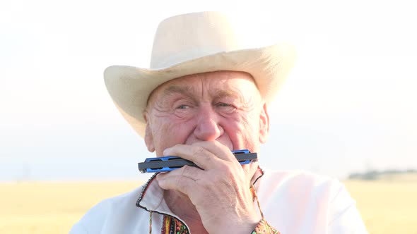 An Old Man in an Embroidered Coat and Hat Plays the Harmonica