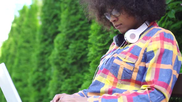 Portrait African American Woman with an Afro Hairstyle Uses a Laptop Sitting on Bench on the Street