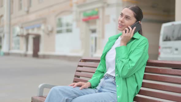 Hispanic Woman Talking on Phone While Sitting Outdoor on Bench
