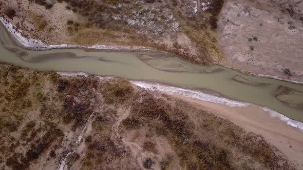 Aerial view following murky river flowing through the desert