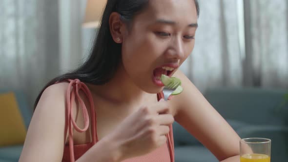 Asian Woman With A Dish Of Healthy Food Using A Fork Poking Cucumber Before Eating At Home