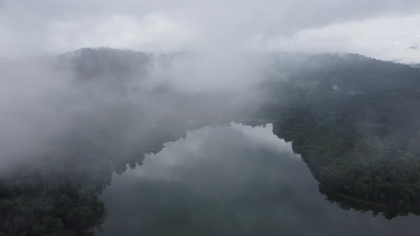 Aerial fly away low cloud of lake at tropical rainforest