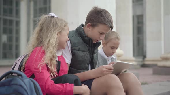 Positive Caucasian Schoolboy Resting with Classmates on School Stairs. Side View of Carefree Boy and