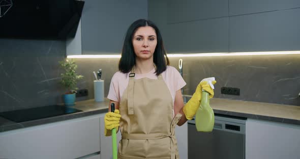 Housewife Wearing Rubber Gloves, Holding Bottle of Cleaning Spray and Mop at Kitchen home