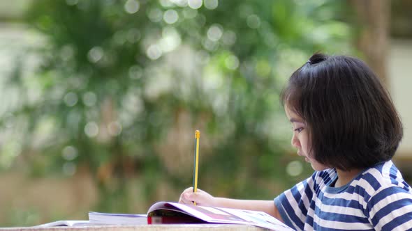 Little Asian girl doing homework in the garden.