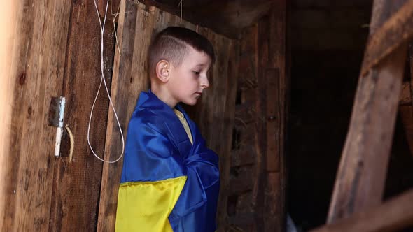 sad Ukrainian small child stands outdoors supporting homeland, little kid covered in national flag. 