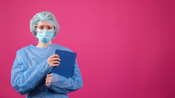 Serious Doctor in a Blue Medical Coat Safety Glasses and Medical Cap Looking at Camera