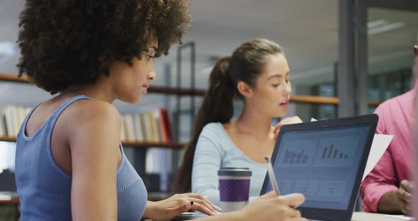 Diverse male and female business colleagues talking and using laptop