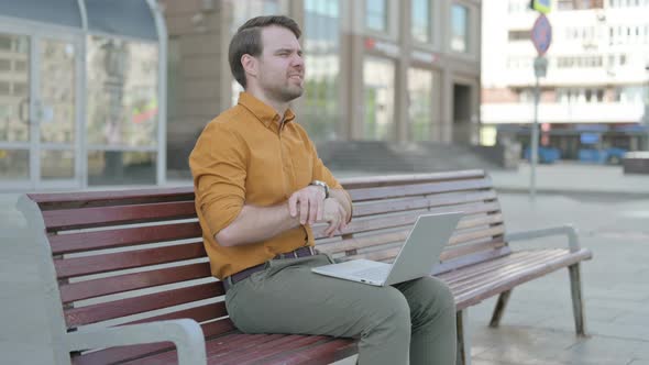 Young Man with Wrist Pain Using Laptop while Sitting on Bench
