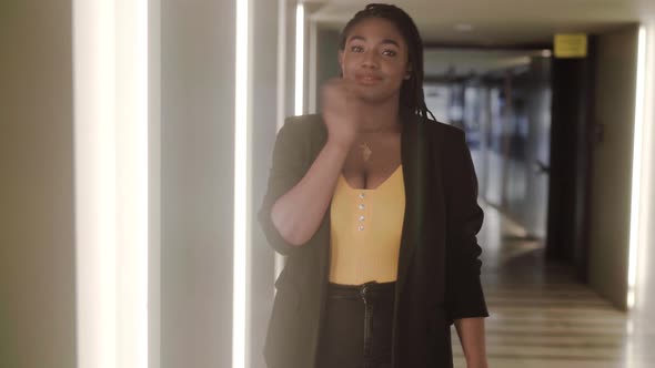 Stylish black woman putting on jacket while walking in hall