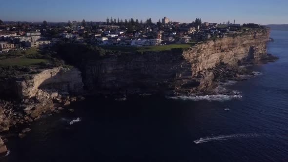 Beautiful scenic aerial reverse flight reveals the ocean coastal cliff and a single fishing boat app