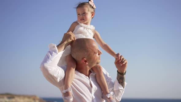 Cute Caucasian Little Girl Sitting on Shoulders of Man Looking Around with Clear Blue Summer Sky at