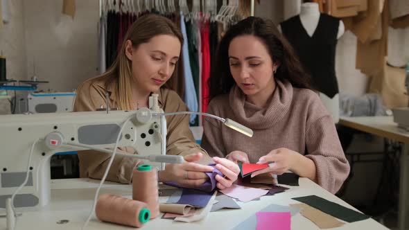 Two femail fashion designers looking at samples of sketches in a sewing workshop studio