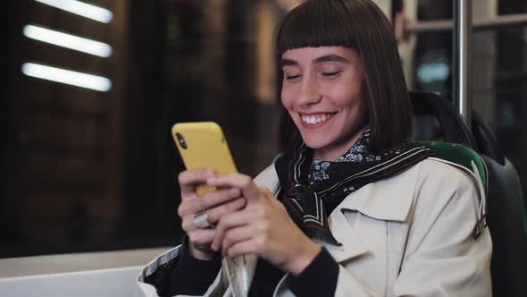 Smiling Young Woman Watching Video on the Smartphone at Public Transport. Night Time. Close-up. City