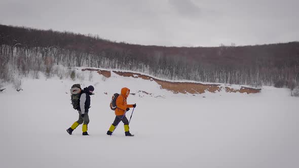 Side View Shot of Two Adventurous Men with Backpacks and Ski Poles Coming Through Deep Snow Layer