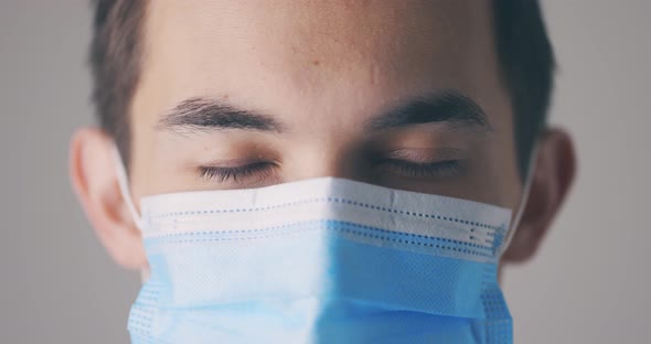 Young Male in Medical Mask Opening Eyes and Looking Straight to Camera