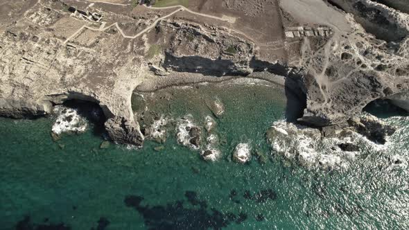 Ancient cliffside ruins overlook turquoise blue Mediterranean waters. Summertime Milos Greece 4k.