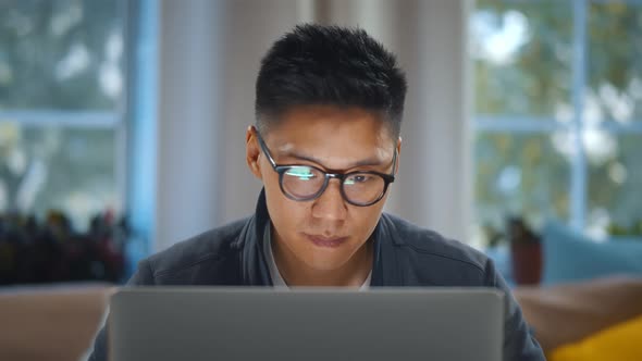 Close Up of Young Asian Man in Glasses Working on Laptop at Home Office