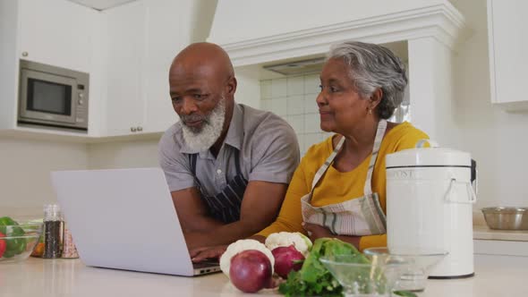 African american senior couple wearing aprons using laptop together in the kitchen at home