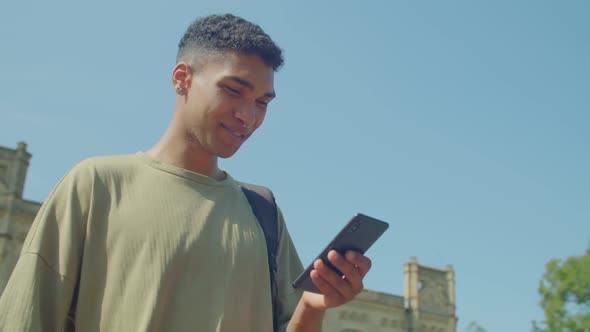 Portrait of Smiling Black Male Text Messaging Online on Cellphone Outdoors