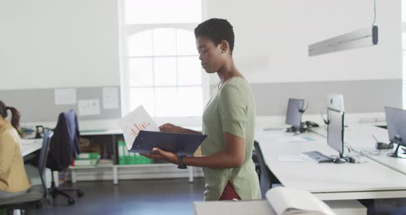 African american businesswoman walking in office and looking on documents