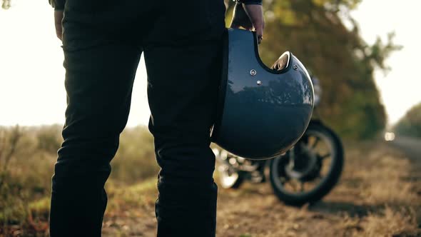 Back View of an Unrecognizable Man in Black Jeans and Leather Jacket Holding His Helmet in His Hand