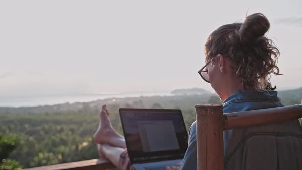 Freelancer woman sits with a laptop on a high bar chair. 