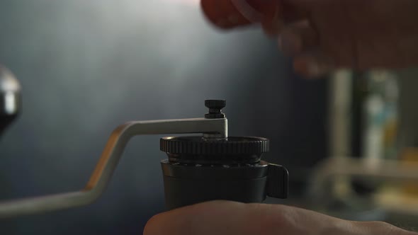 Hand Twists the Handle of a Mechanical Coffee Grinder in the Kitchen at Home